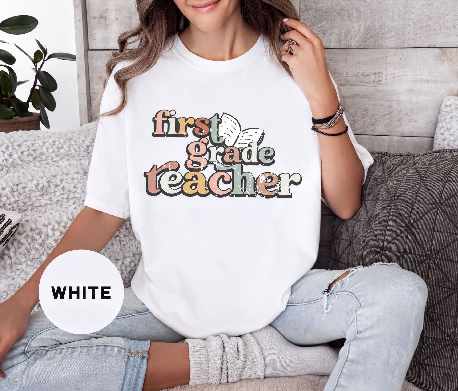 A woman wearing a white t-shirt with the text "first grade teacher" printed on it, sitting on a couch.