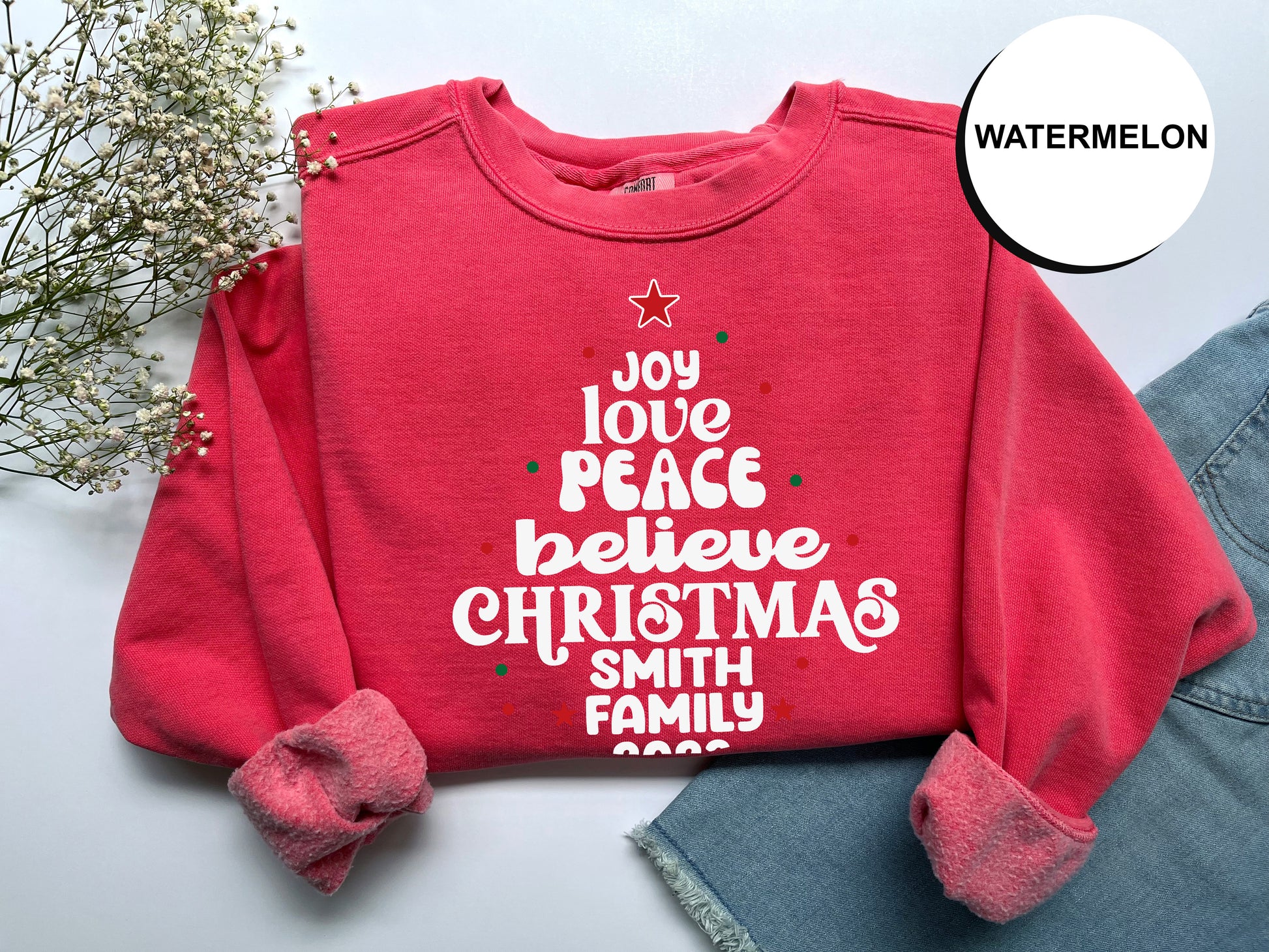 A red sweater with white text and a star on it, along with some flowers and a denim skirt, is displayed on a white background.