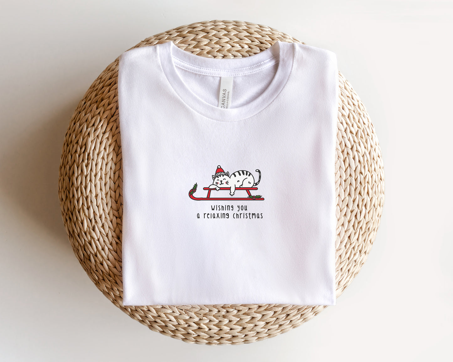 A white t-shirt with a graphic design of a cat on a sled, along with the text "Wishes you a relaxing christmas".