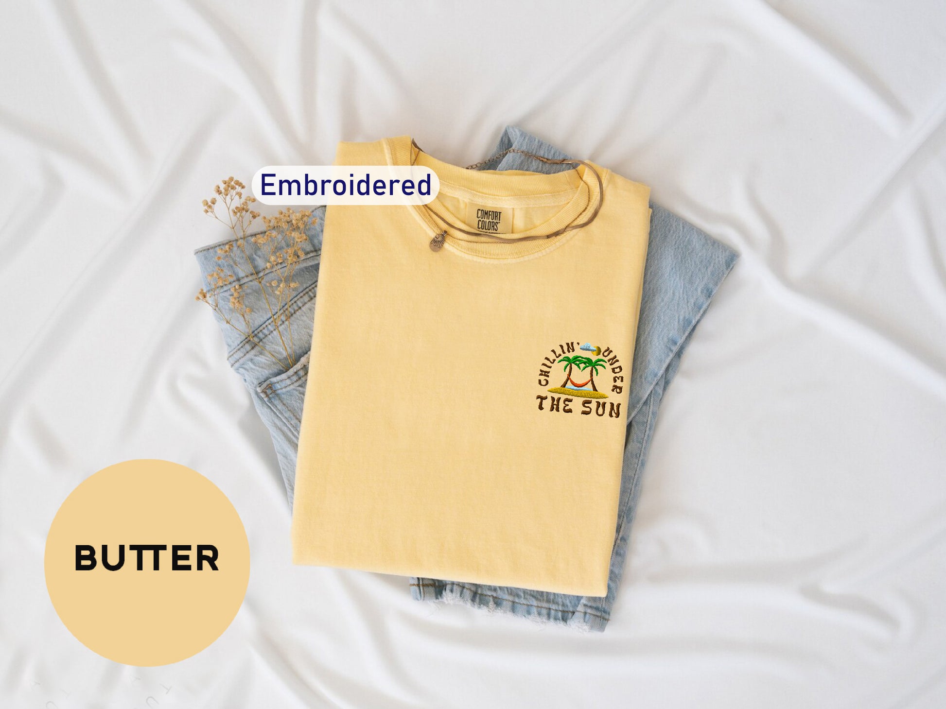 a yellow t-shirt with a graphic design, a pair of blue jeans, and a small plant, all laid out on a white background.
