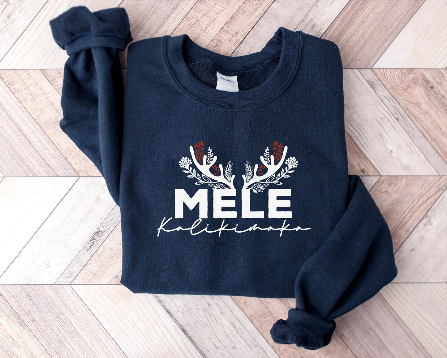 A navy blue sweatshirt with white text and decorative elements, such as antlers and flowers, is displayed on a wooden surface.