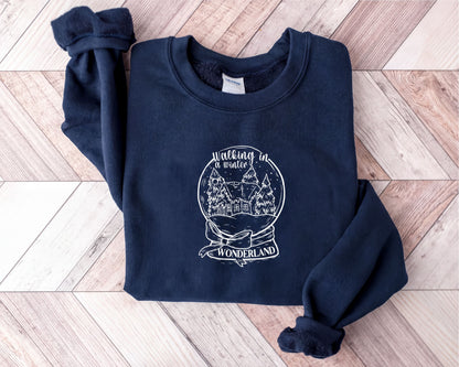 A navy blue sweatshirt with a white graphic design on it, depicting a snow globe with a castle and trees, along with the text "Walking in Wonderland".