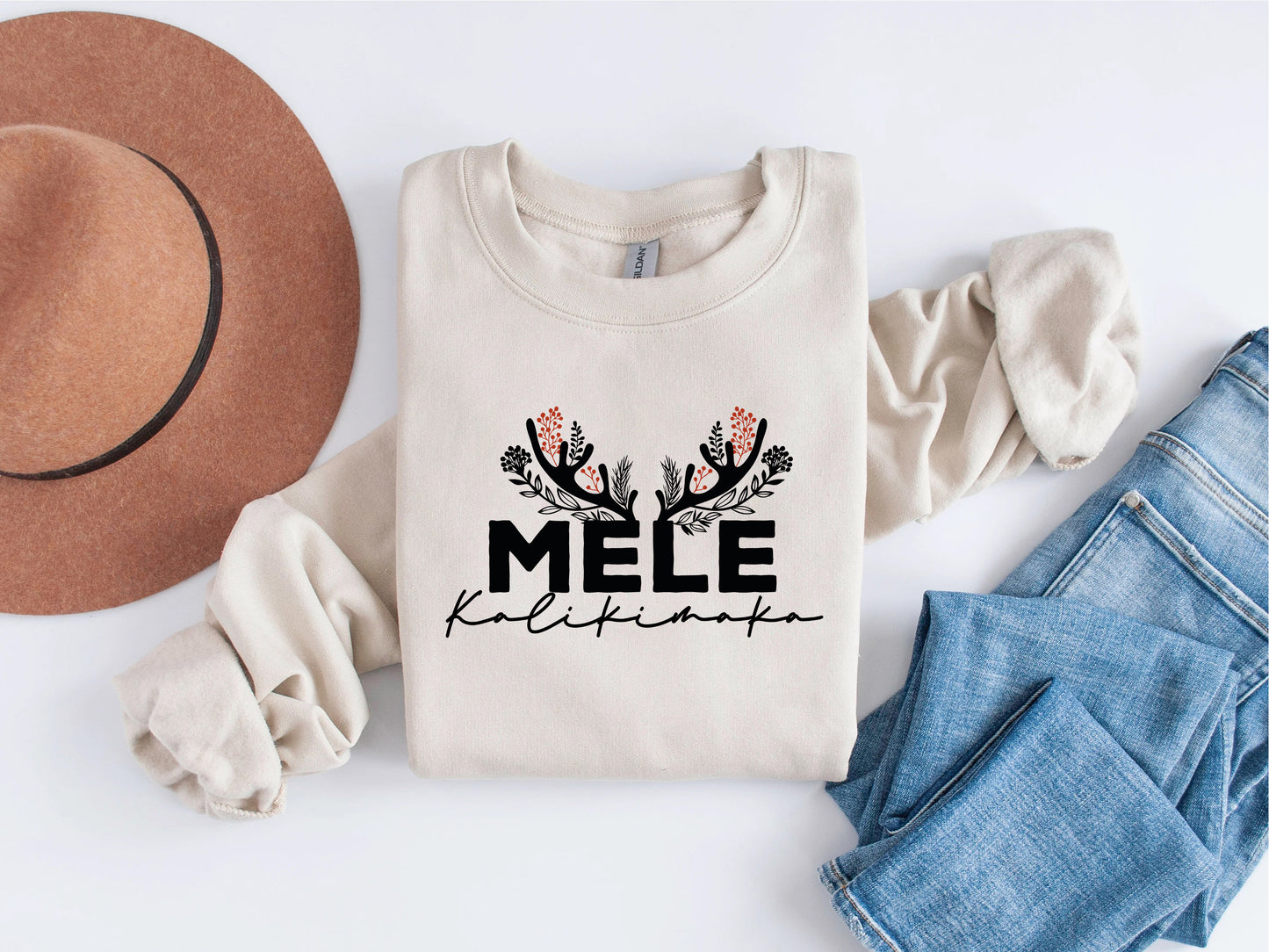 A beige sweater with the text "MELE Kalikimaka" printed on it, along with a brown hat and blue jeans, all laid out on a white background.