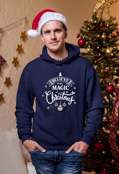 A man wearing a navy blue hoodie with a Christmas-themed design stands in front of a decorated Christmas tree.