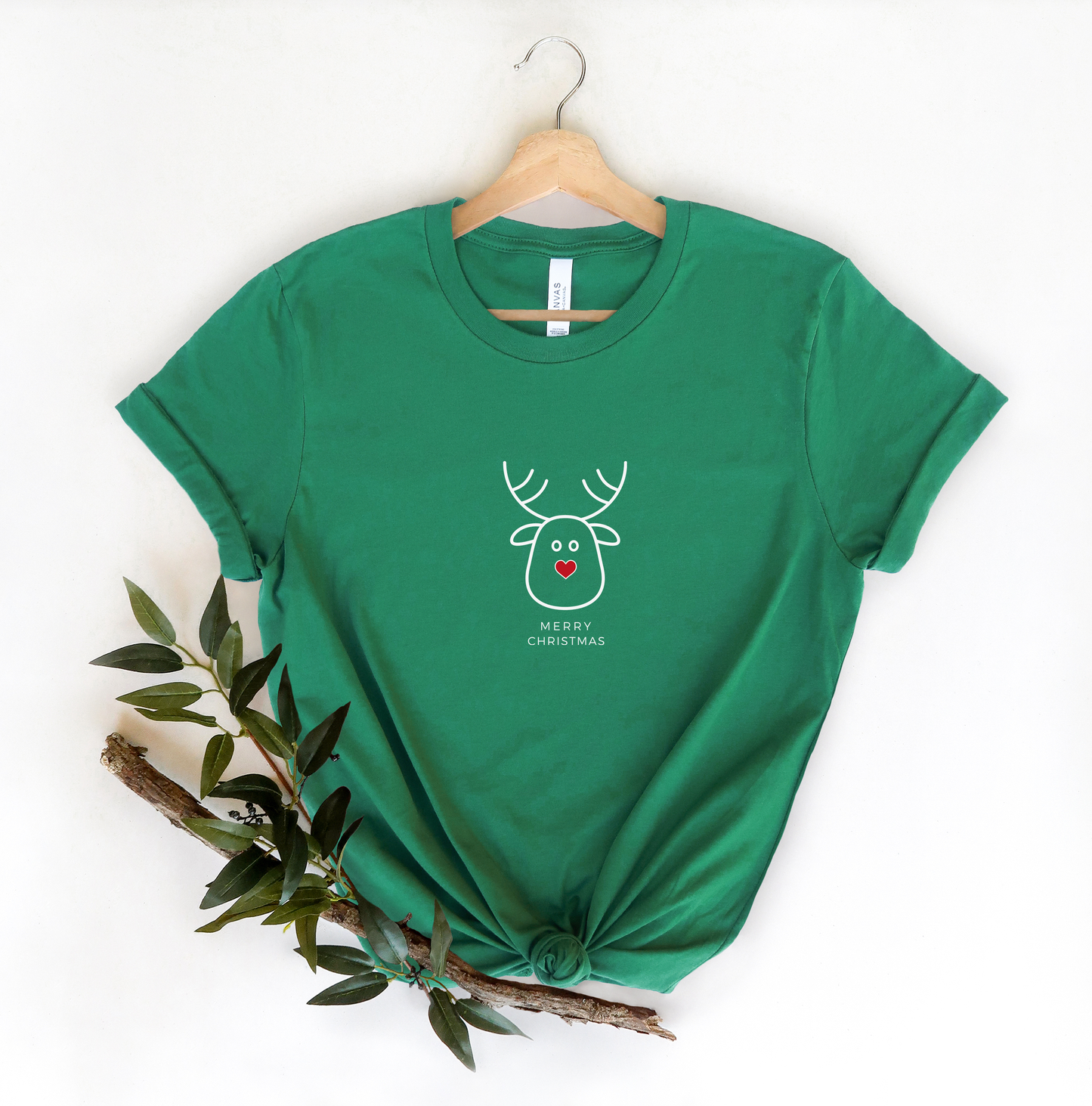A green t-shirt with a white reindeer graphic and the text "Merry Christmas" printed on it, hanging on a wooden hanger.