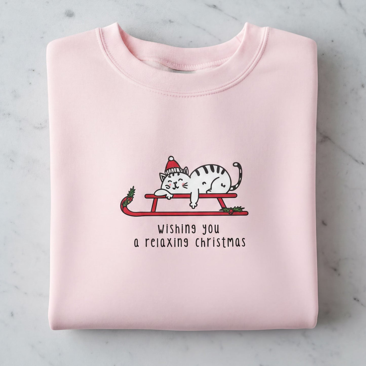 A pink sweatshirt with a graphic of a cat wearing a Santa hat and a sled, along with the text "Wishing you a relaxing christmas".