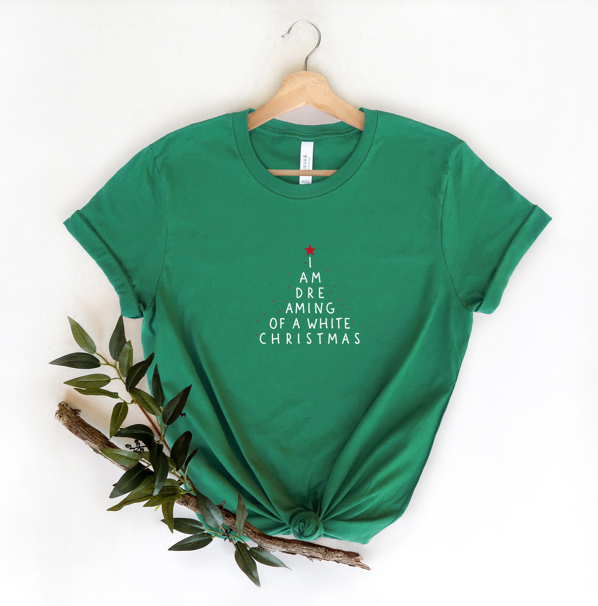 A green t-shirt with white text that says "I AM DREAMING OF A WHITE CHRISTMAS" is hanging on a wooden hanger.