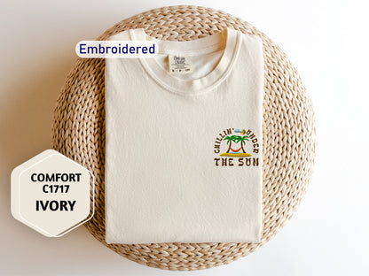 a white t-shirt with a tropical design, laid out on a woven basket. The t-shirt has a label that reads "Embroidered" and "Comfortable C1717 Ivory".