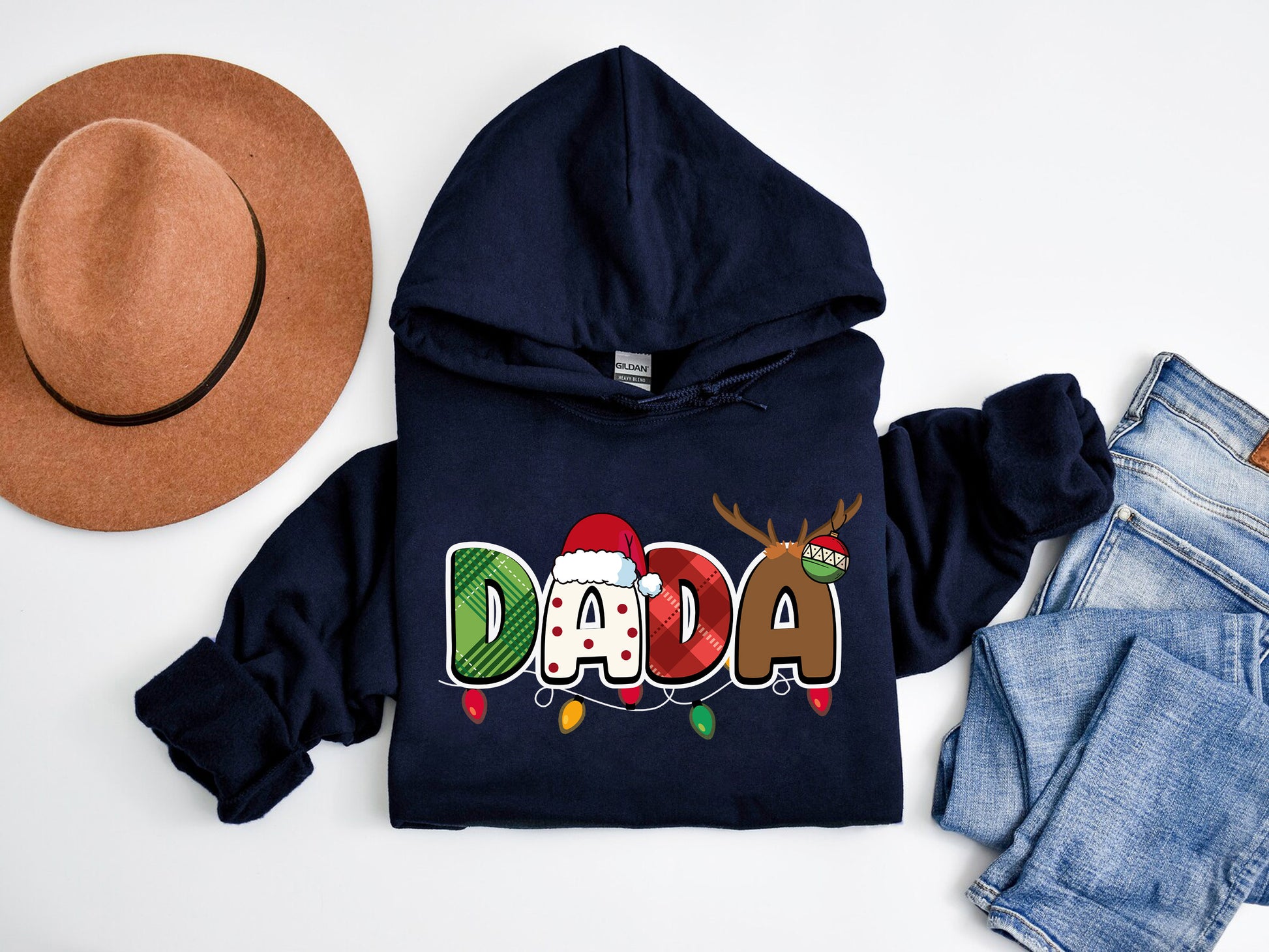 A navy blue hoodie with the word "DADA" printed on it, along with a brown hat and a pair of jeans, are laid out on a white background.