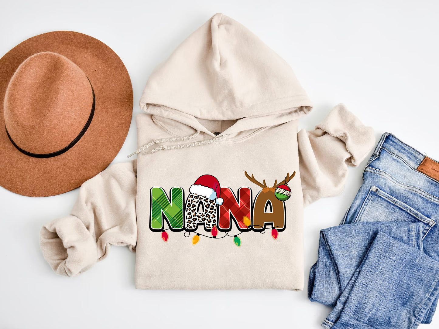 A beige hoodie with a Christmas-themed design, a brown hat, a pair of jeans, and a pair of socks are arranged on a white background.