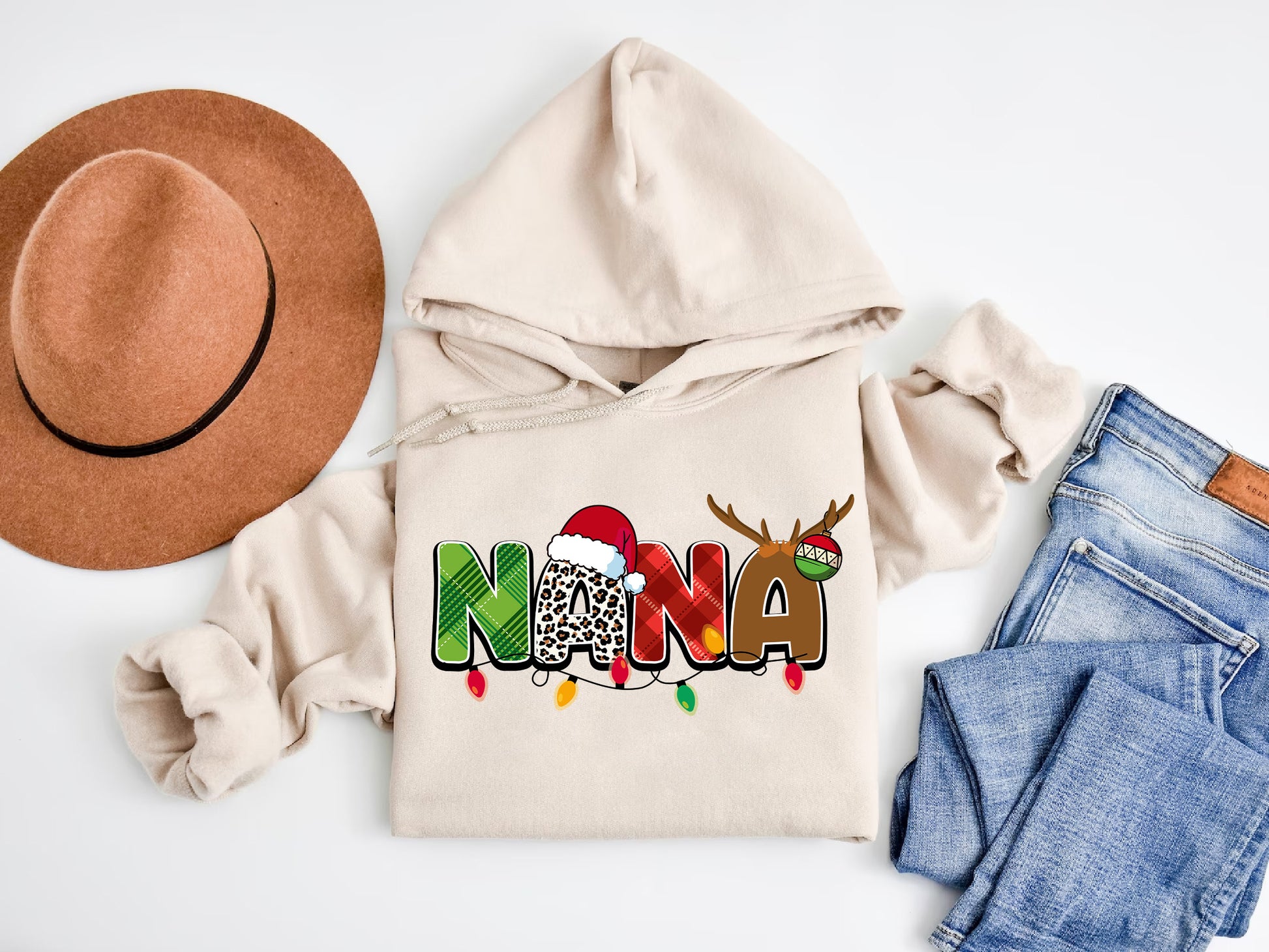 A beige hoodie with a Christmas-themed design, a brown hat, a pair of jeans, and a pair of socks are arranged on a white background.