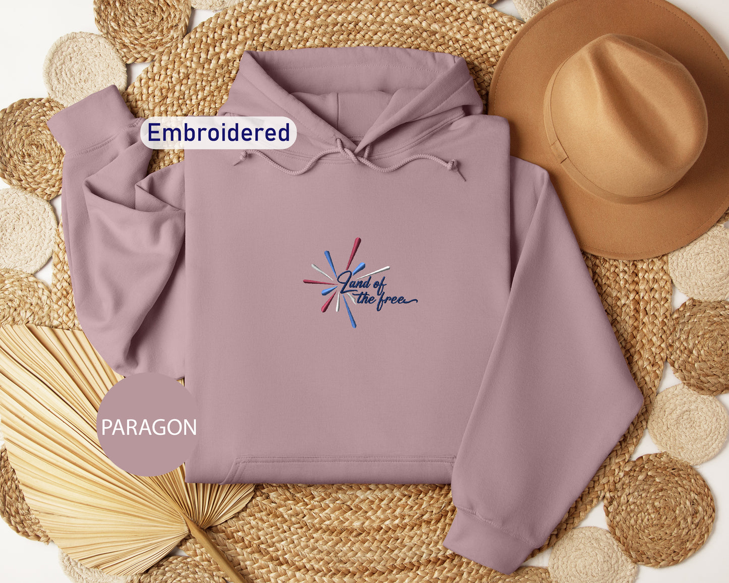 a purple hoodie with a patriotic design, a brown hat, and a woven straw hat, all arranged on a woven mat.