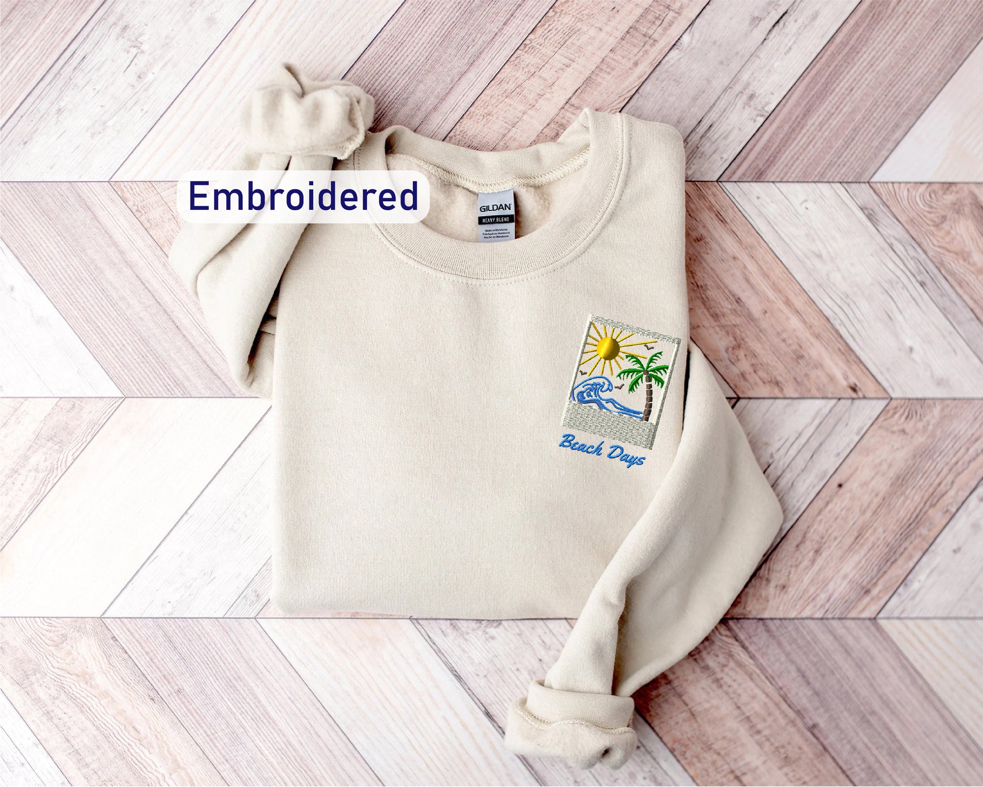 A beige sweater with a small embroidered patch on the front, placed on a wooden surface.