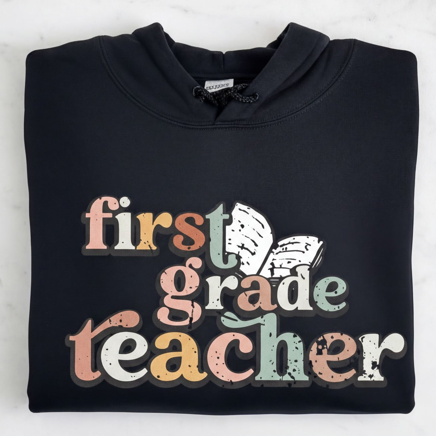 A black hoodie with the text "first grade teacher" printed on it.