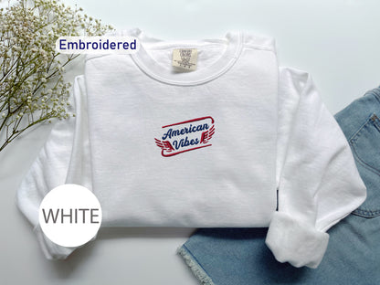 a white long-sleeved shirt with a red and blue logo, laid out on a white surface alongside a pair of denim jeans.