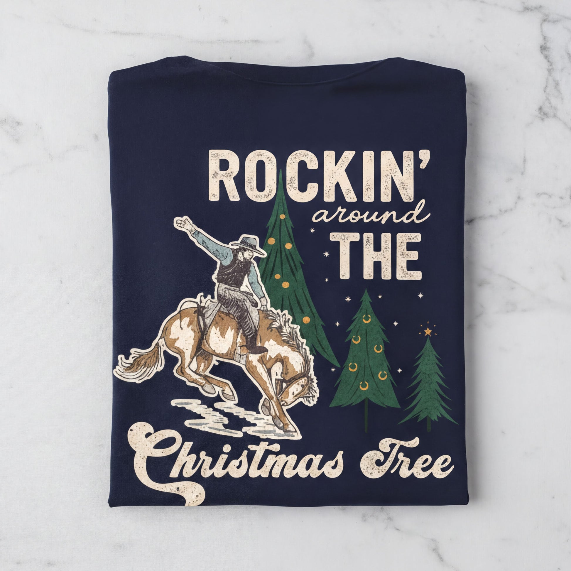 The image is a t-shirt design featuring a cowboy riding a bucking bronco, with Christmas trees and the phrase "Rockin' around the Christmas Tree" written on it.