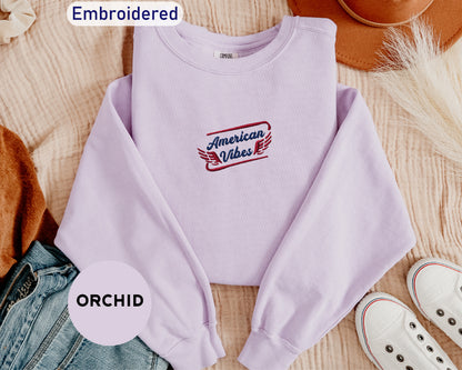 a purple sweatshirt with an embroidered design, a pair of jeans, a brown hat, and a pair of white sneakers, all laid out on a surface.