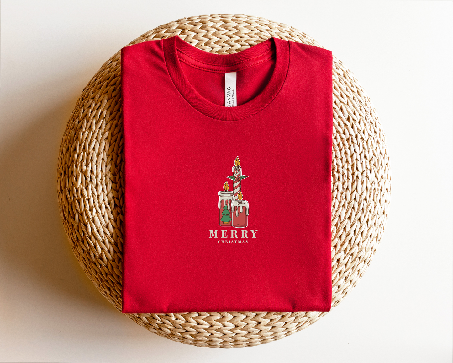 A red t-shirt with a graphic design of a character and the text "MERRY CHRISTMAS" printed on it, placed on a woven basket.