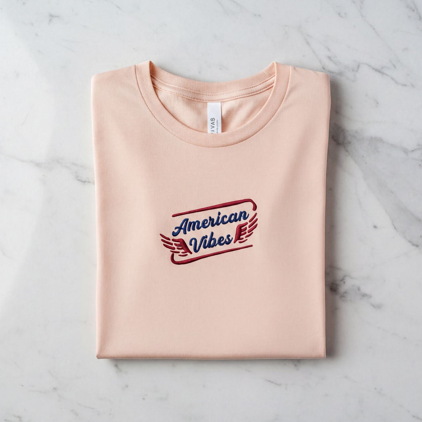 A pink t-shirt with the text "American Vibes" printed on it, laid out on a marble surface.