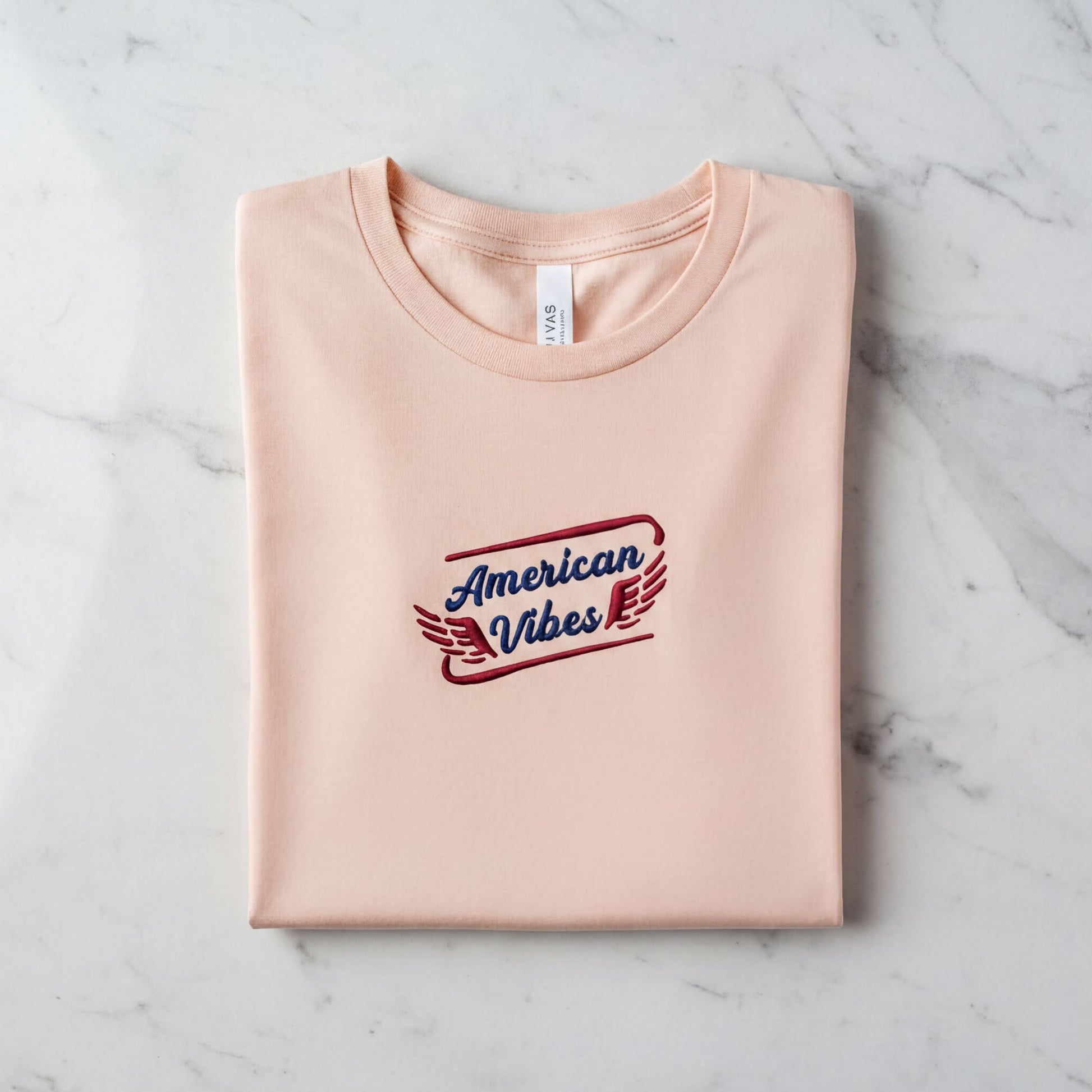 A pink t-shirt with the text "American Vibes" printed on it, laid out on a marble surface.