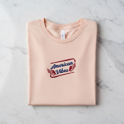 A pink t-shirt with the text "American Vibes" printed on it, laid out on a marble surface.
