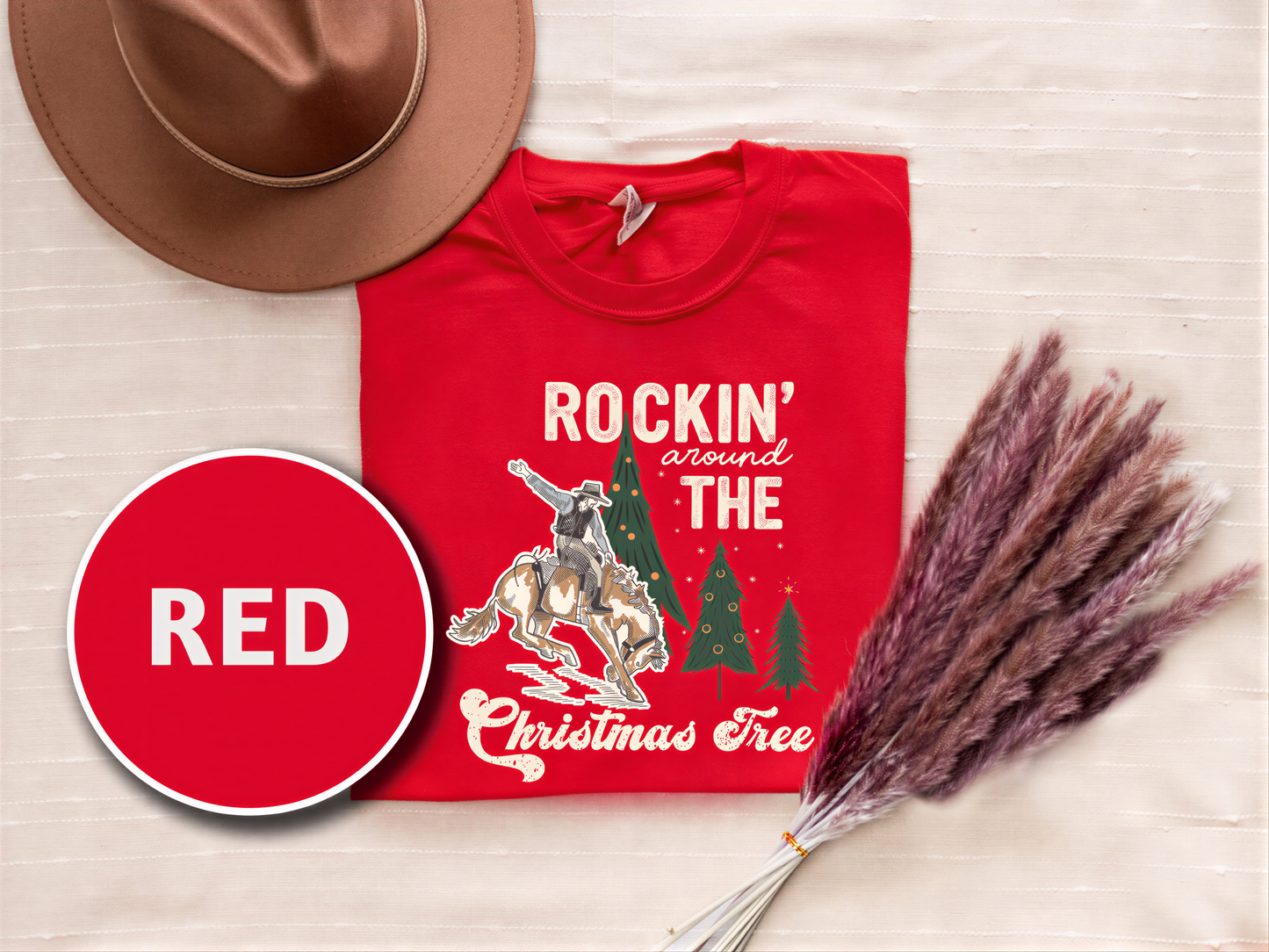 a red t-shirt with a cowboy graphic and the phrase "ROCKIN' around THE CHRISTMAS Tree" printed on it, along with a brown hat and some purple reeds.