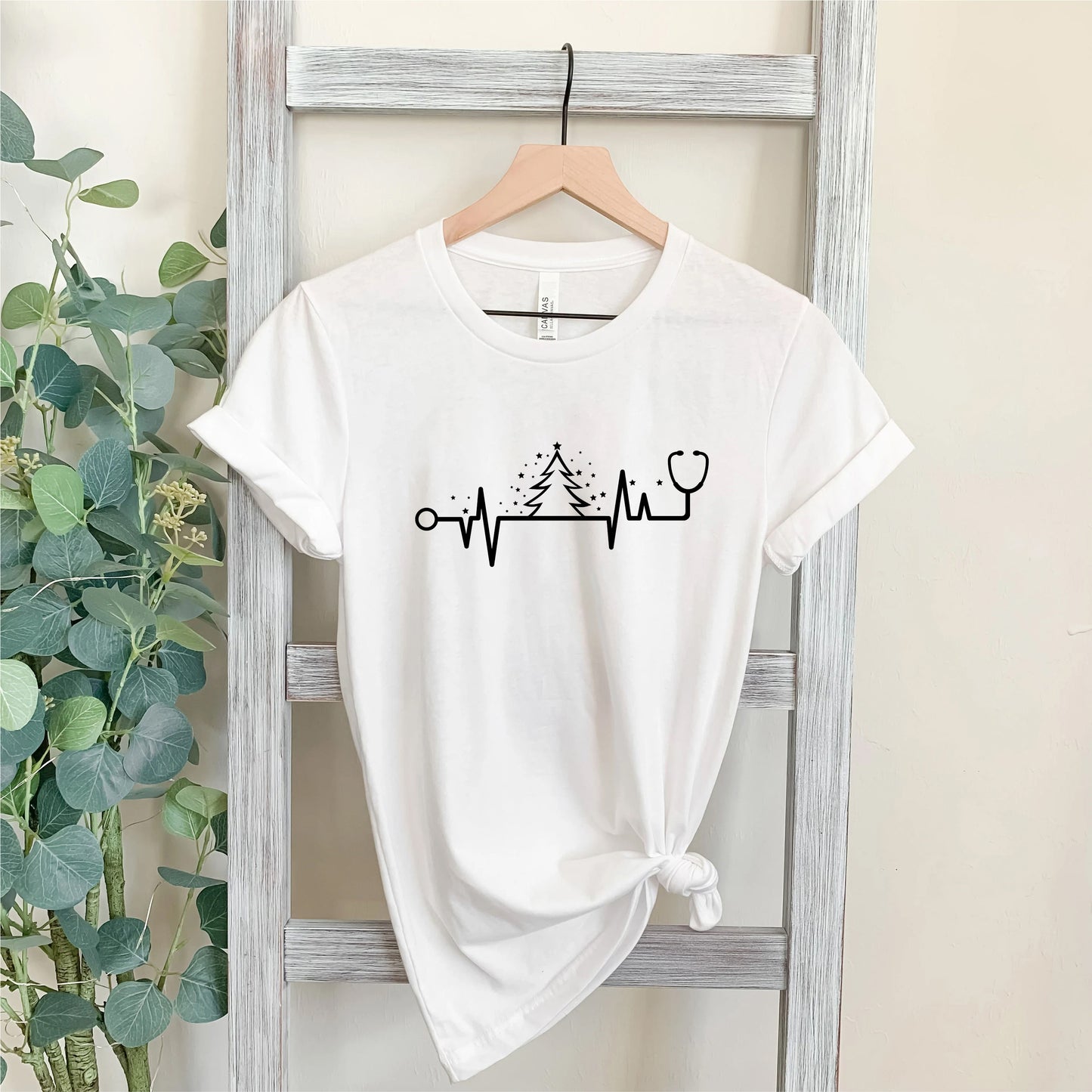 A white t-shirt with a graphic design on it, hanging on a wooden hanger.