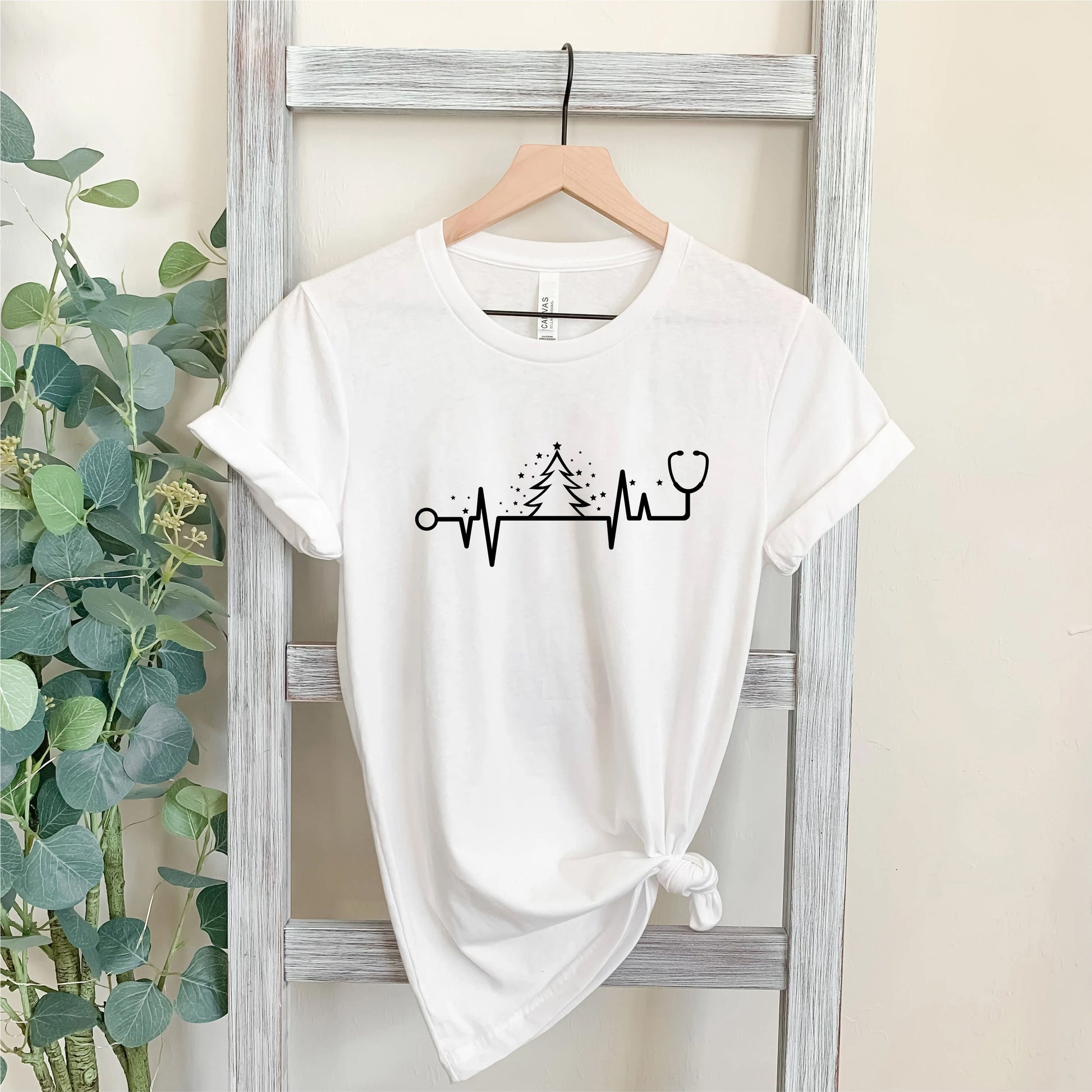 A white t-shirt with a graphic design on it, hanging on a wooden hanger.