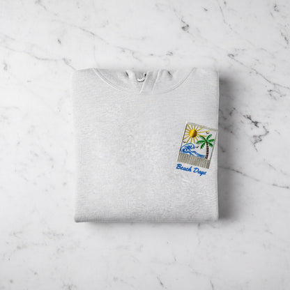 A white hoodie with a beach-themed design and the text "Beach Days" printed on it, laid out on a marble surface.