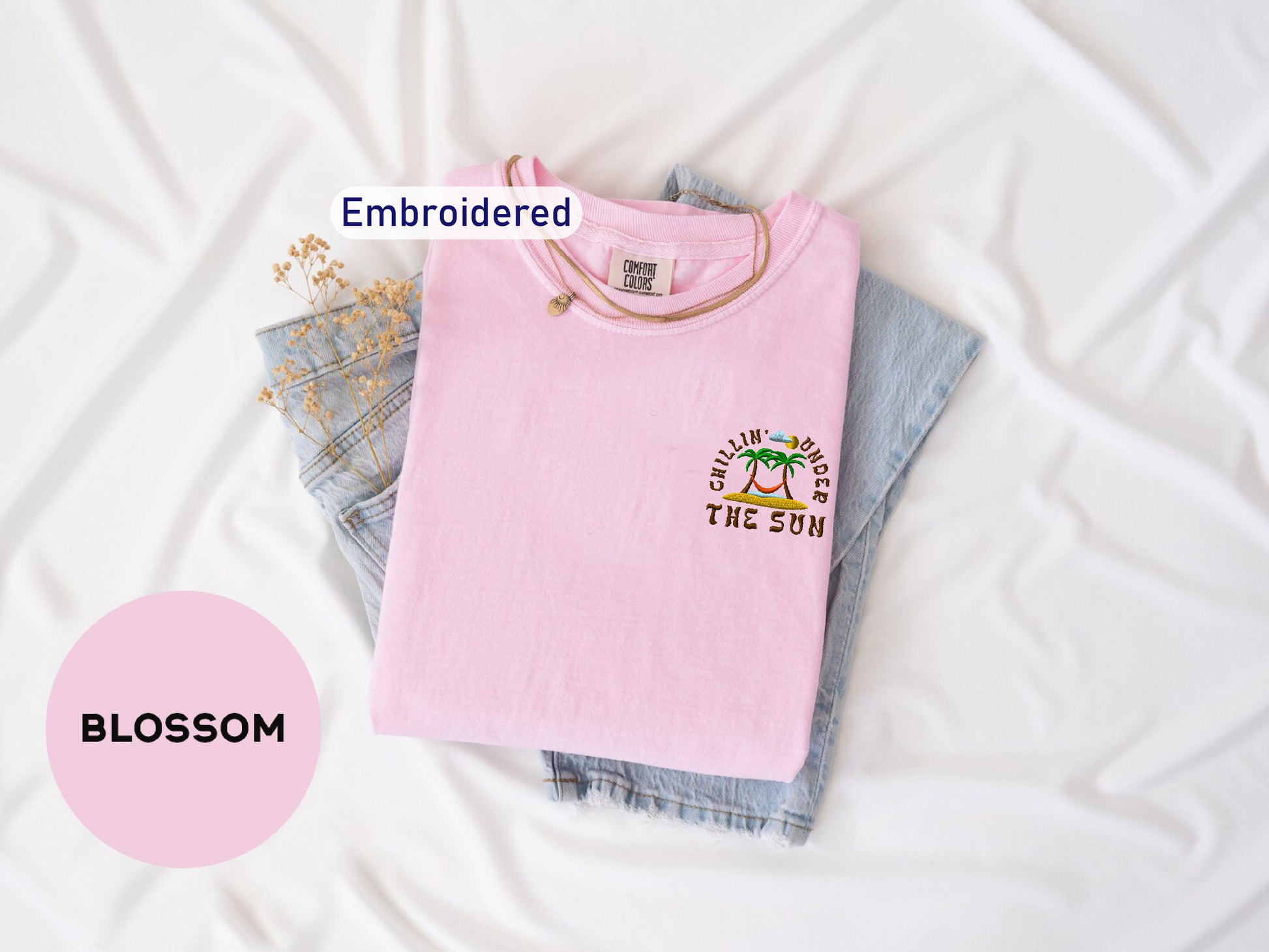 a pink t-shirt with a graphic design, a pair of denim jeans, and some dried flowers, all laid out on a white surface.