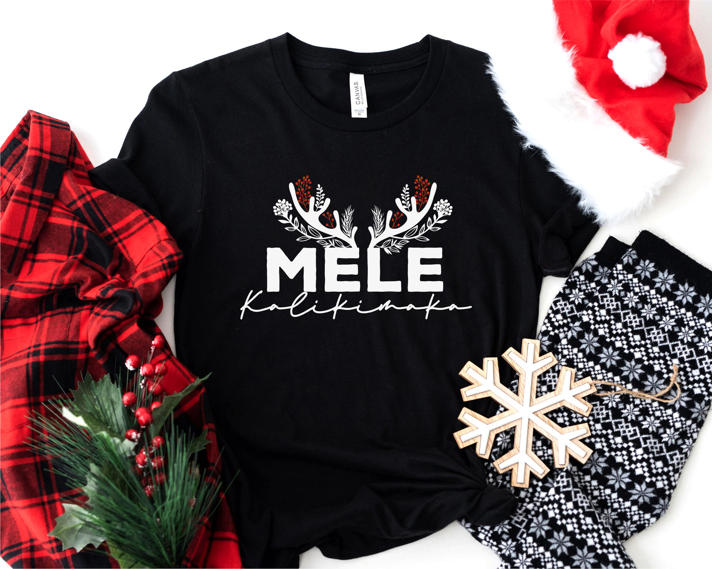A black t-shirt with the text "MELE Kalikimaka" printed on it, along with a red and black plaid shirt, a Santa hat, a snowflake ornament, and a pair of pajama pants.