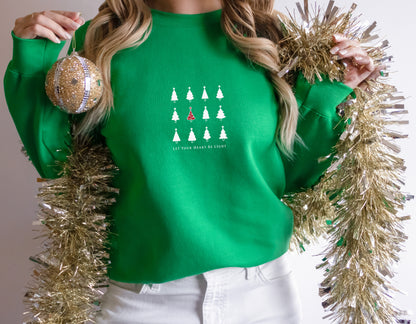 A woman wearing a green sweater with a Christmas tree design and holding a gold ornament and a gold tinsel garland.