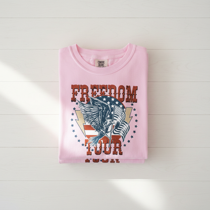 A pink t-shirt with a graphic design featuring an eagle and the text "FREEDOM TOUR" printed on it.