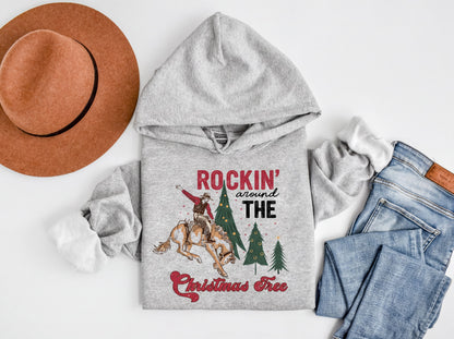 A gray hoodie with a graphic design, a brown hat, a pair of jeans, and a Christmas tree, all laid out on a white background.