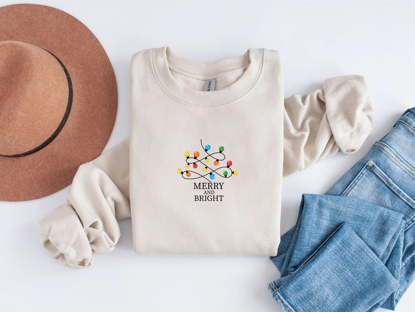A beige sweater with a Christmas-themed design, a brown hat, and a pair of blue jeans are arranged on a white background.