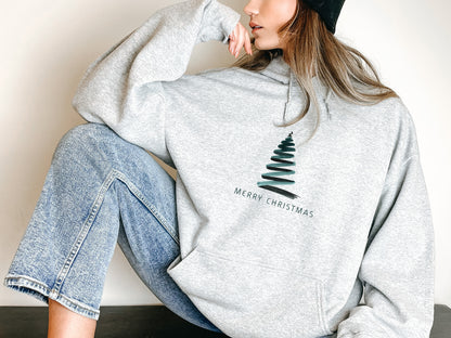 A woman wearing a grey hoodie with a Christmas tree design and the text "Merry Christmas" printed on it.