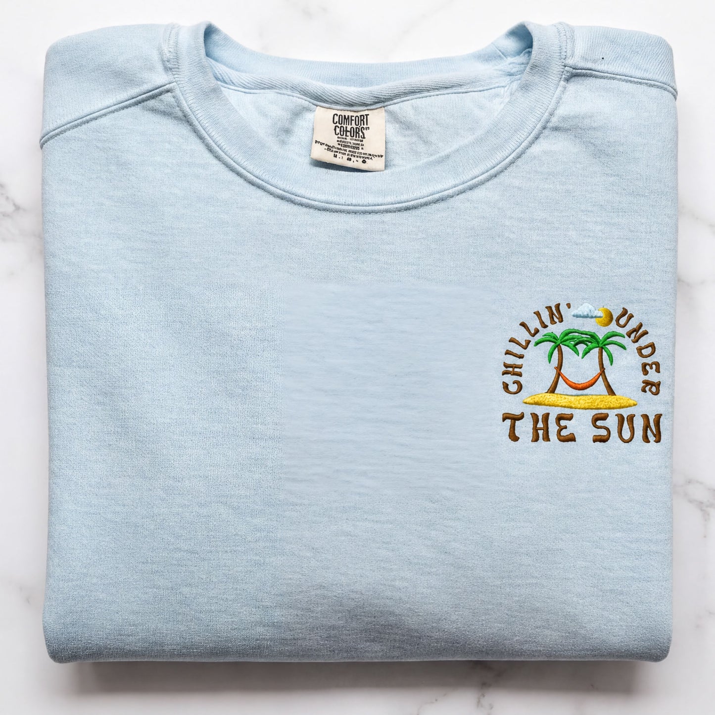 A light blue t-shirt with a printed design on the front, featuring a palm tree and the text "Chillin' under the sun".