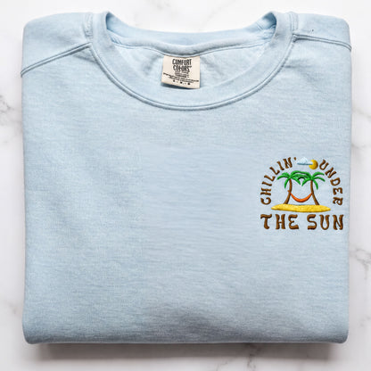 A light blue t-shirt with a printed design on the front, featuring a palm tree and the text "Chillin' under the sun".