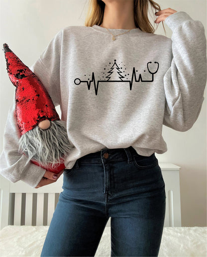 A woman wearing a grey sweatshirt with a graphic design of a Christmas tree and a stethoscope, holding a red sequined gnome.