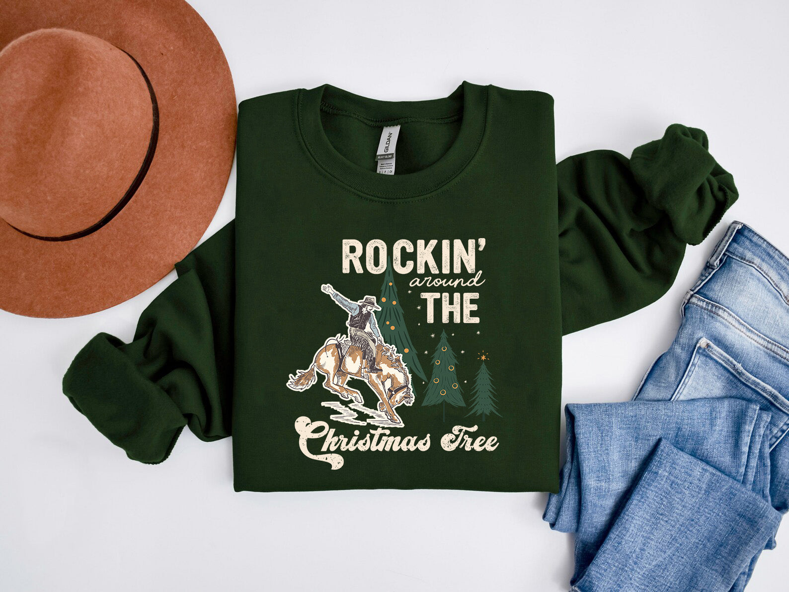 a green sweatshirt with a graphic design, a brown hat, and a pair of blue jeans, all laid out on a white background.