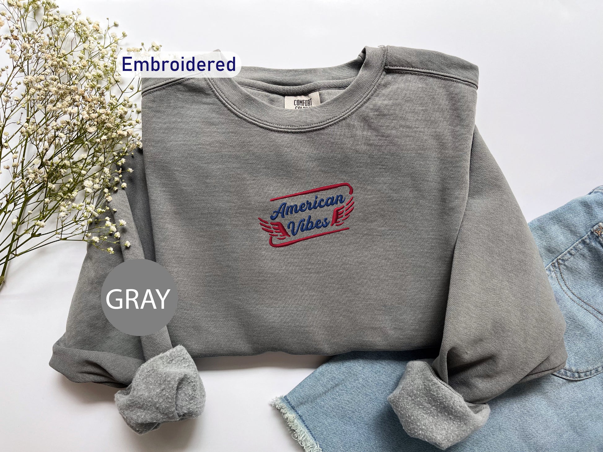 a gray sweatshirt with an embroidered design, a pair of denim jeans, and some flowers.