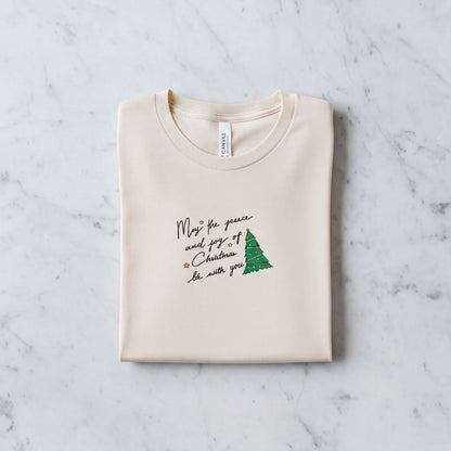 A beige t-shirt with a Christmas-themed design and text printed on it, laid out on a marble surface.