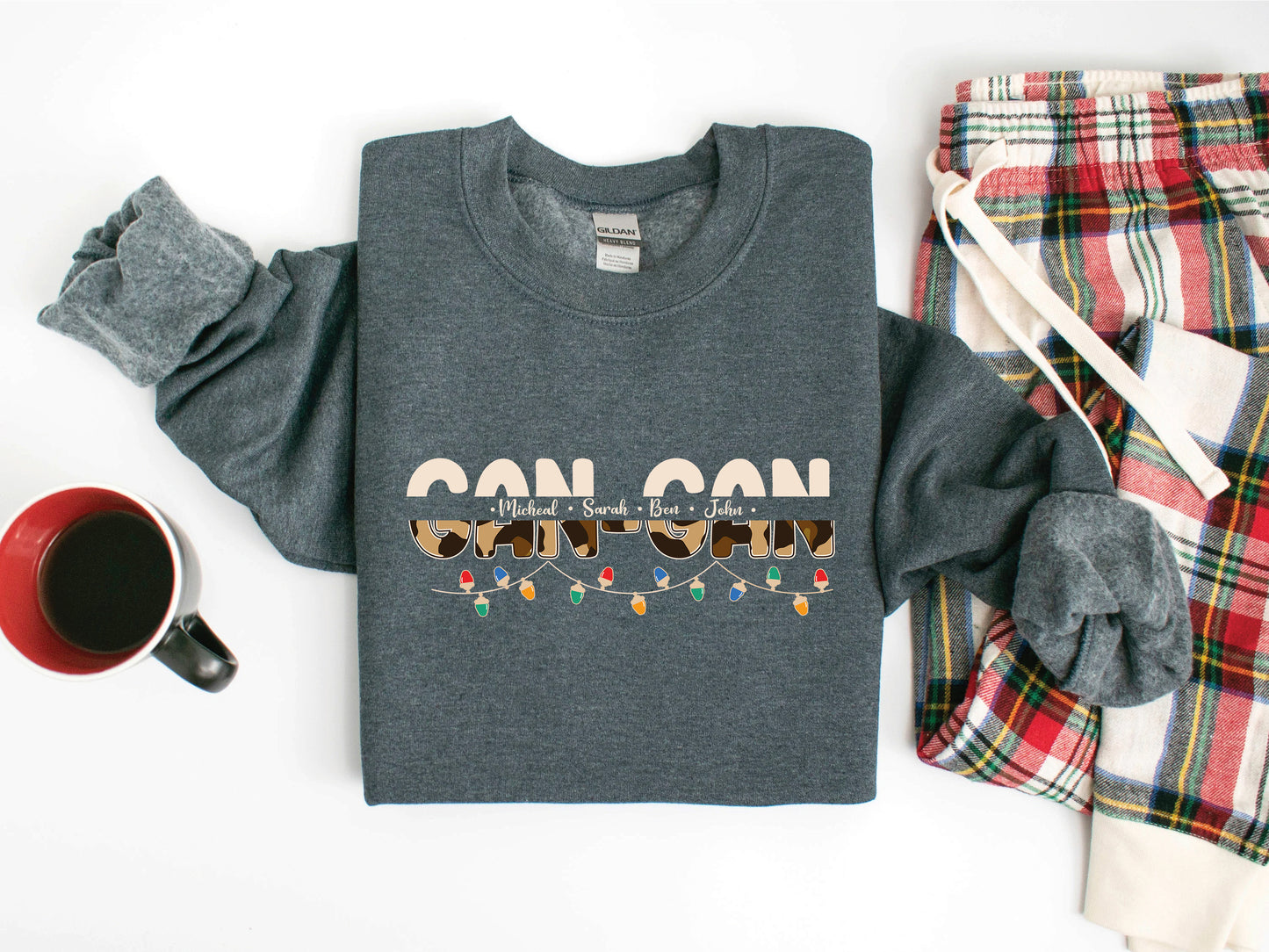 A gray sweatshirt with a graphic design, a pair of plaid pajama bottoms, a red mug, and a pair of gray sweatpants are arranged on a white background.