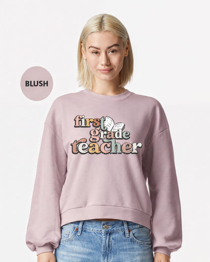 A woman wearing a pink sweatshirt with the text "first grade teacher" printed on it.