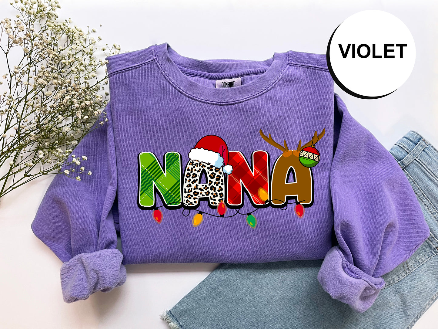 A purple sweatshirt with the word "NANA" printed on it, along with a Santa hat and Christmas lights, is displayed on a white background.