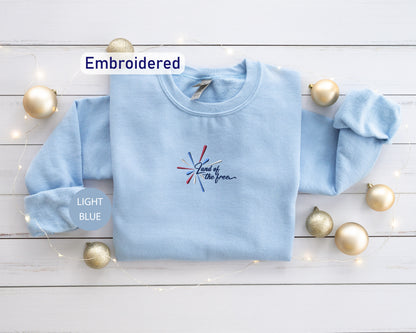 a light blue long-sleeved shirt with a patriotic design, surrounded by gold ornaments and a string of lights on a white wooden surface.