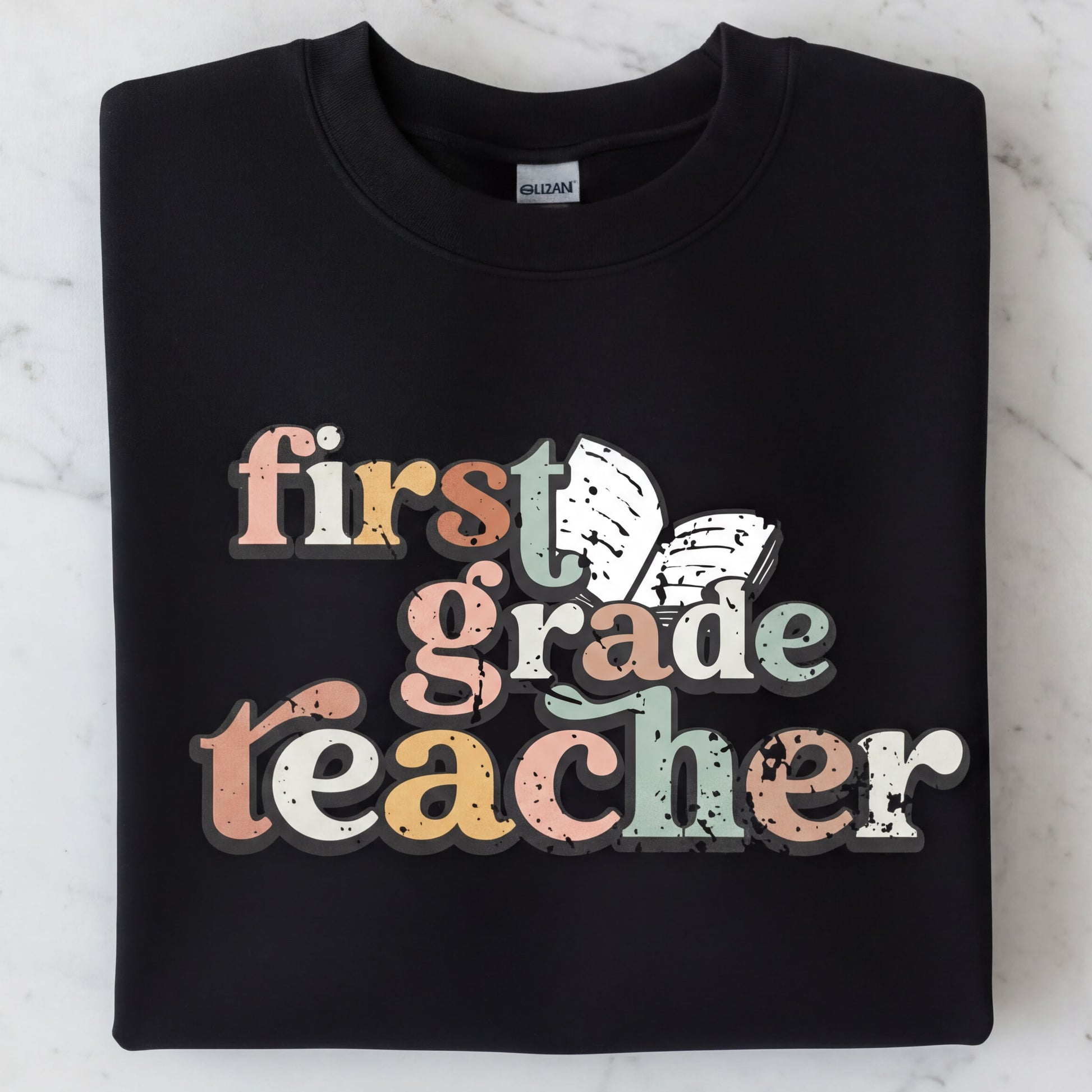 A black sweatshirt with the text "first grade teacher" printed on it in a colorful, distressed font.