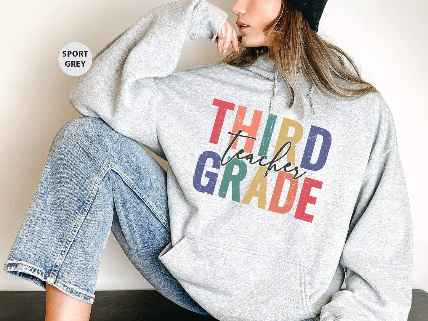 a woman sitting on the ground wearing a sweatshirt that says third grade