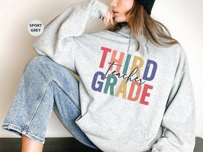 a woman sitting on the ground wearing a sweatshirt that says third grade