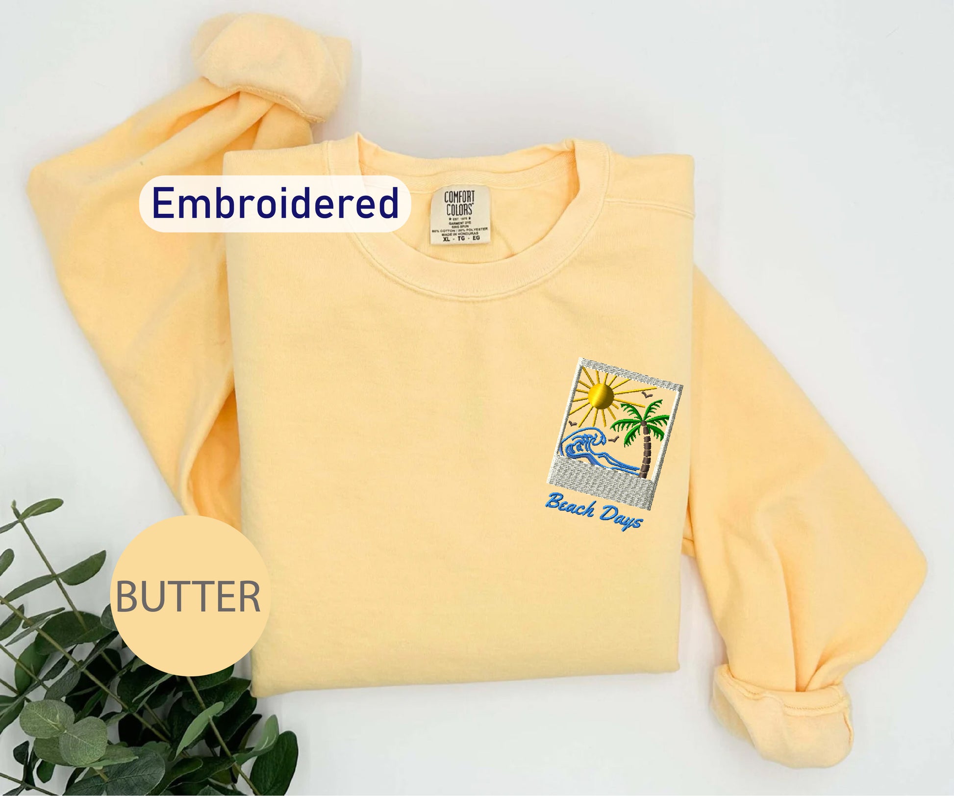 a yellow t-shirt with an embroidered design, including a palm tree and a sun, along with the text "Black Days" and "Butter" printed on it.